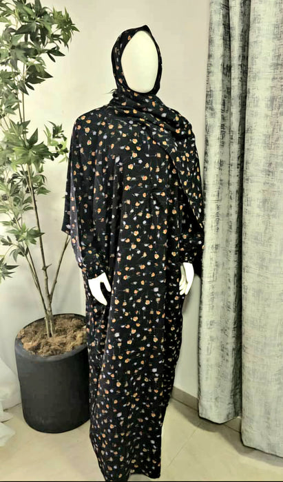 Mannequin wearing a black prayer dress with gold patterns in a room with curtains and a plant.