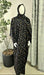 Mannequin wearing a black prayer dress with gold patterns in a room with curtains and a plant.