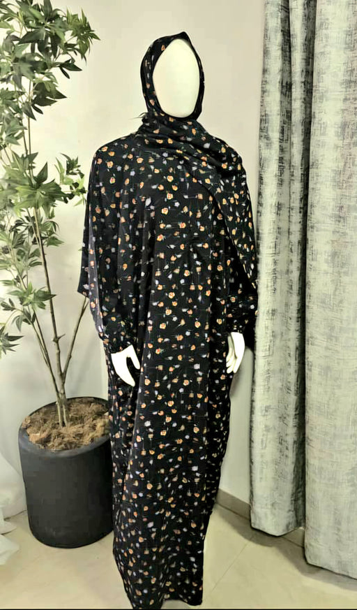Mannequin wearing a black prayer dress with gold patterns in a room with curtains and a plant.