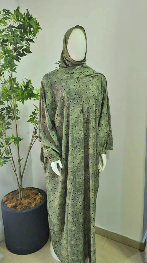 Green patterned prayer dress on a mannequin against a plain wall with a plant in the background